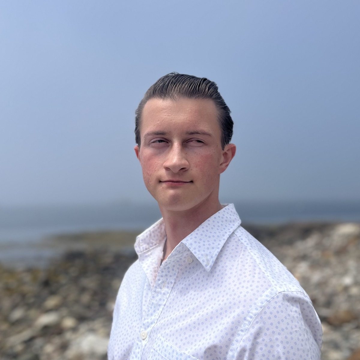Portrait of Samuel Simonds in a white button-up shirt on a rocky shoreline
